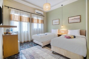 Habitació d'hotel amb dos llits, una taula de treball, una cadira, un televisor i una finestra amb cortines.