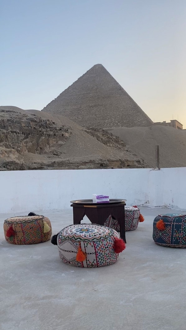 A pyramid, colorful ottomans, and a table with a purple sign on a rooftop.
