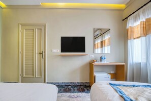 A hotel room with a bed, a TV mounted on the wall, a desk with a computer, and a window with curtains. - Villa Khufu Pyramids Hotel (Giza)