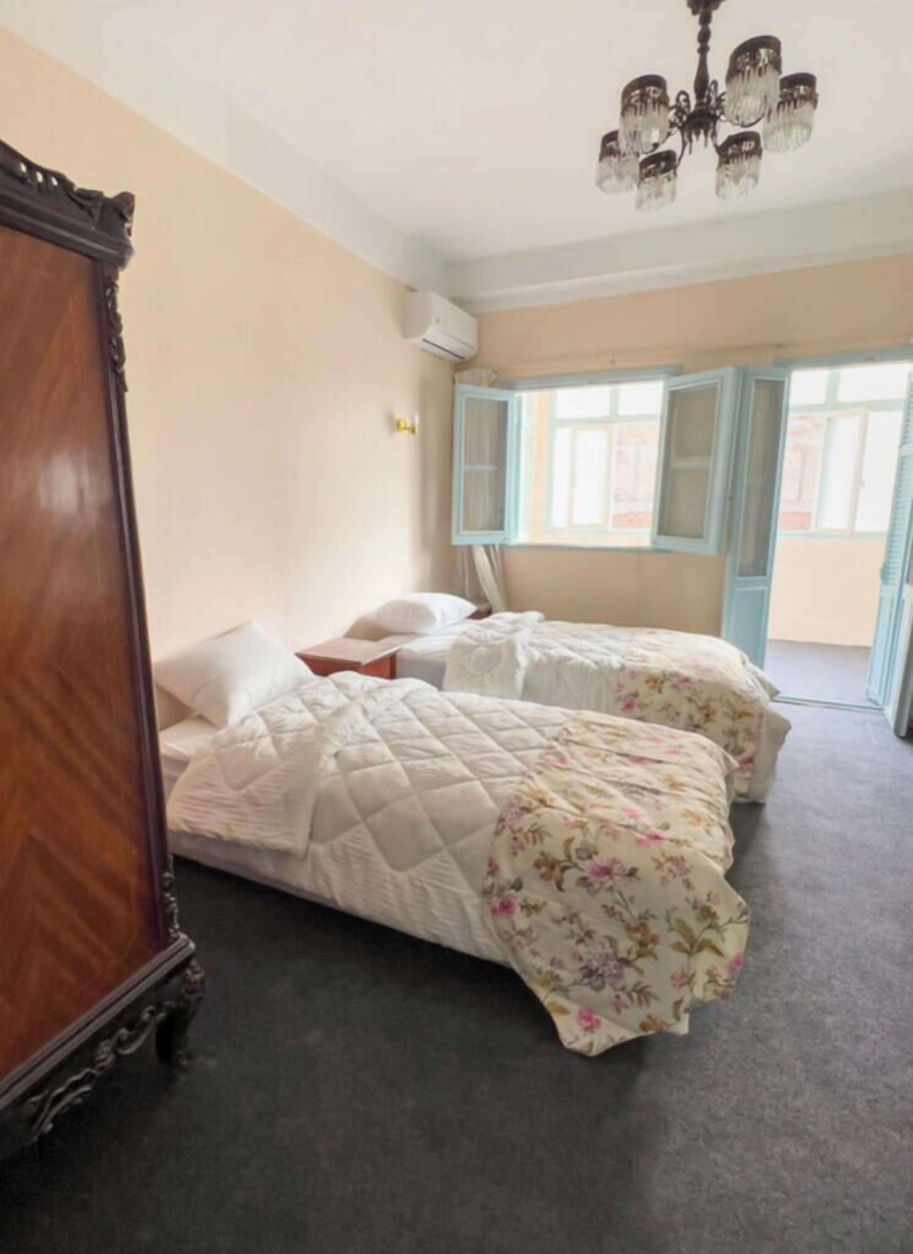 Een kamer met twee bedden, een houten garderobe, een kroonluchter en een raam met gordijnen.