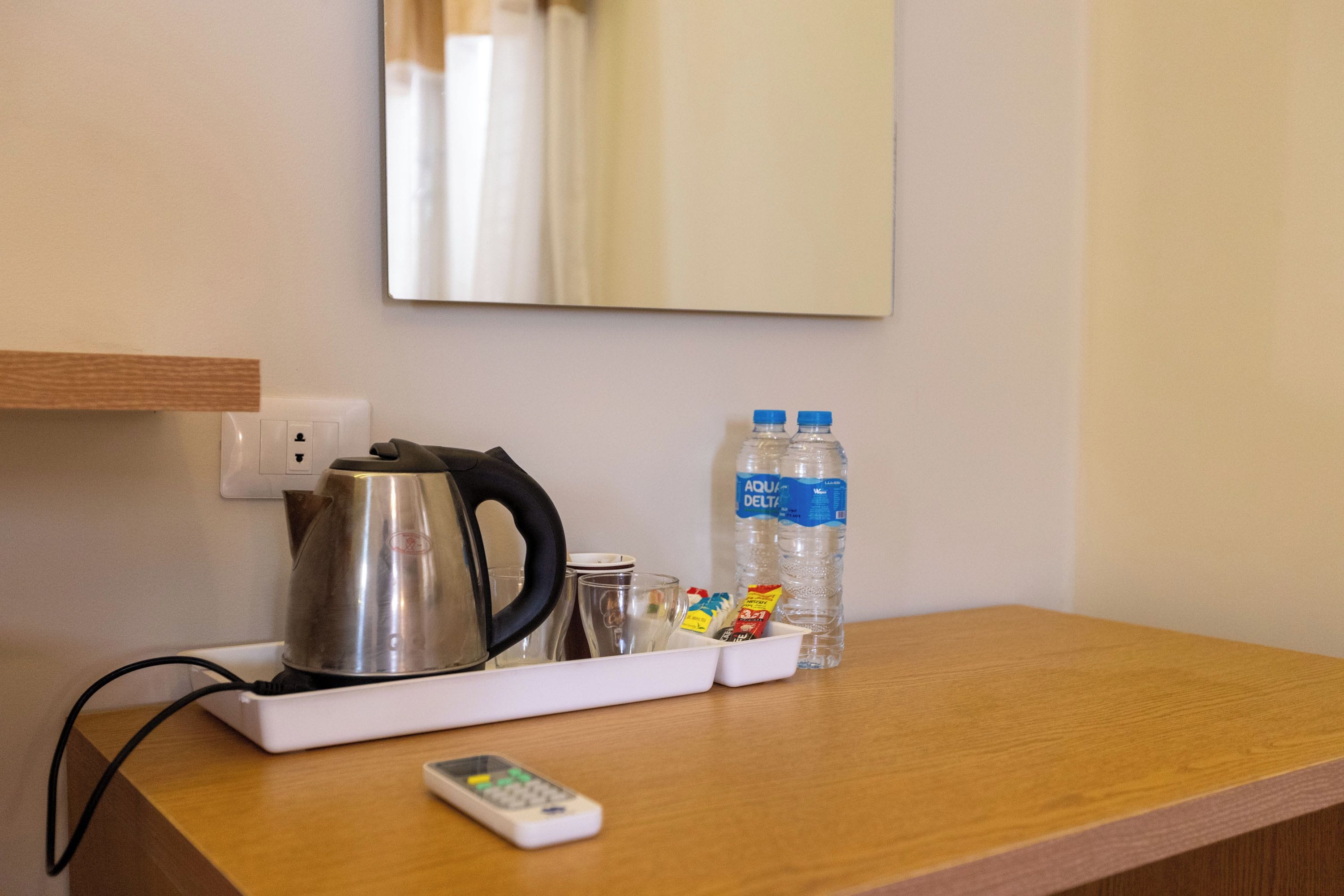 Camera d'albergo con un tavolo in legno, un bollitore, due bottiglie d'acqua, un telecomando e uno specchio a parete.
