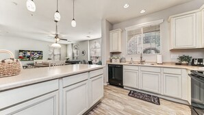 Une cuisine moderne avec des meubles blancs, un grand îlot central, des luminaires suspendus et un revêtement mural au design original.