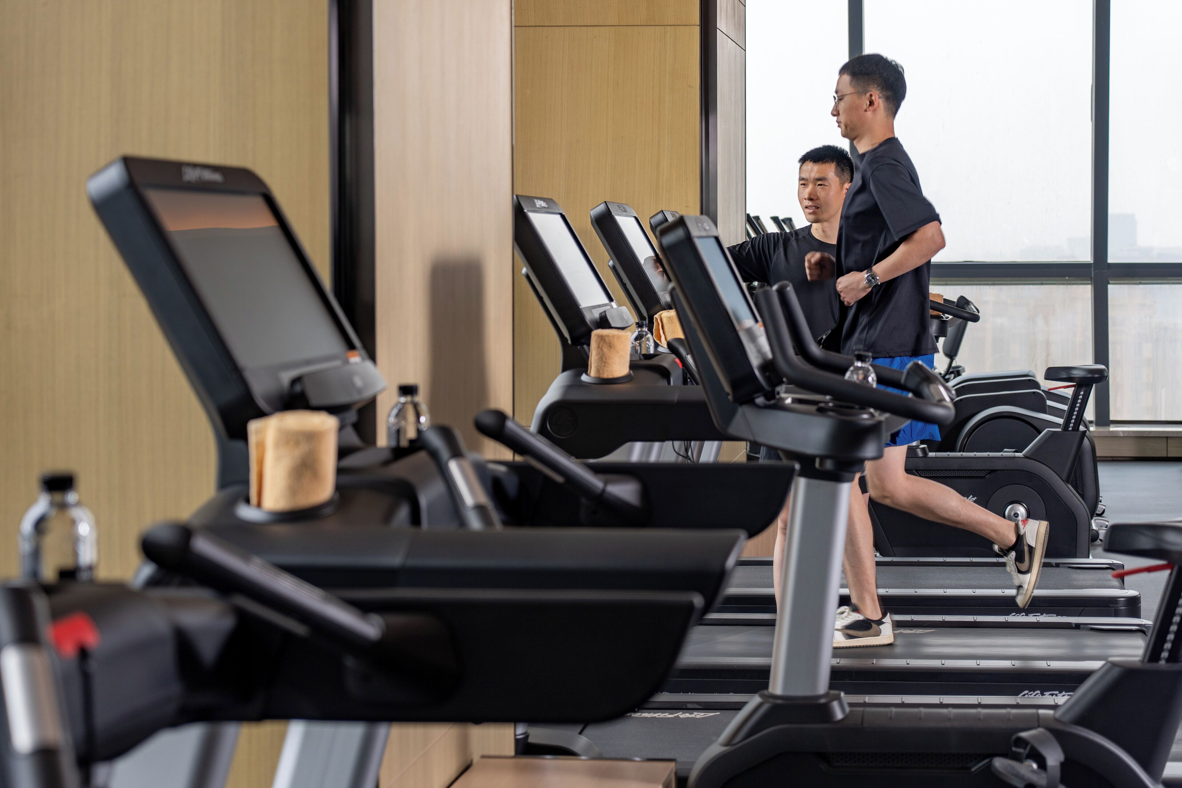 Une salle de sport équipée de tapis de course, d’appareils d’exercice et d’une grande fenêtre laissant entrer la lumière naturelle.
