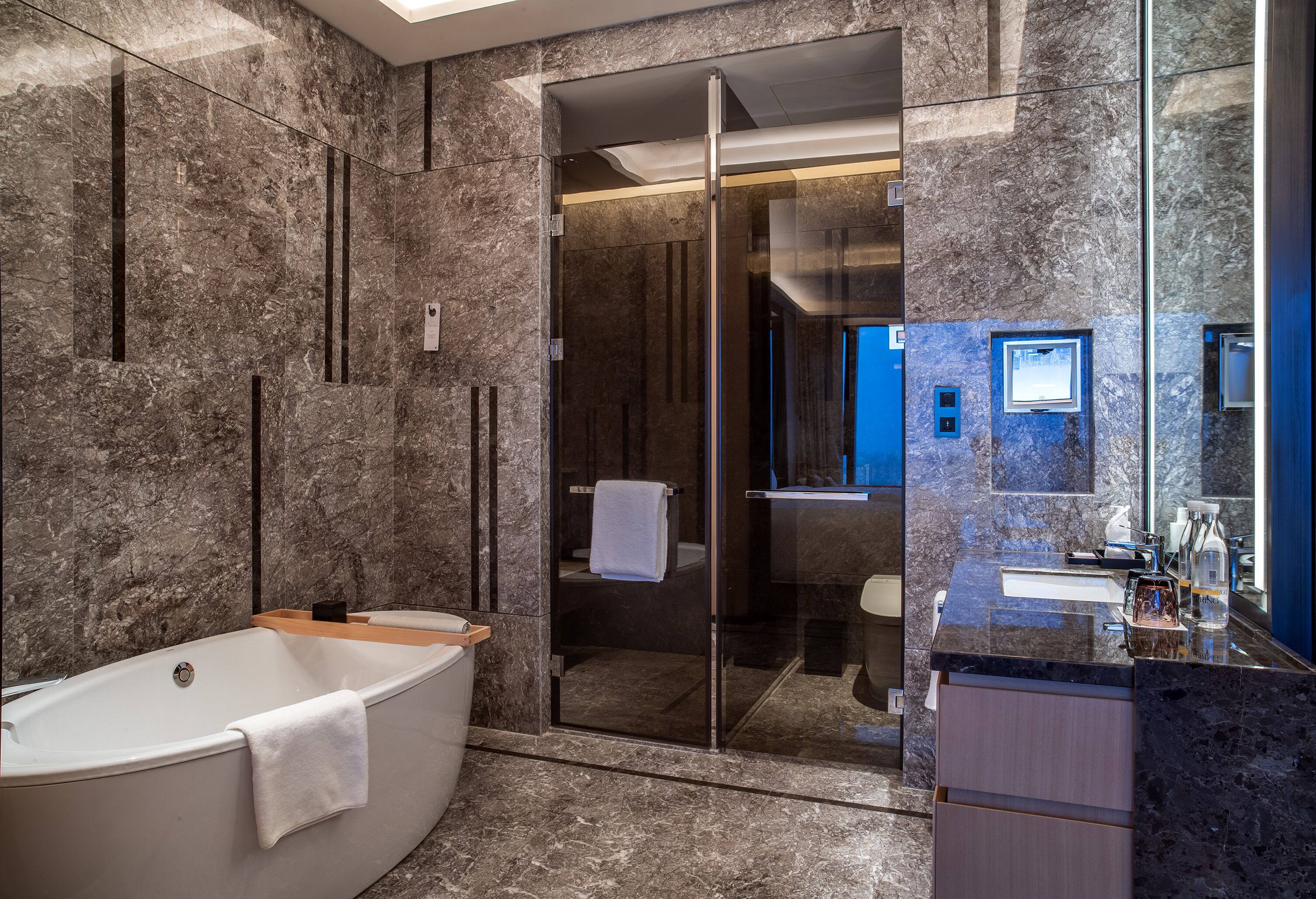 Een moderne badkamer met een vrijstaand bad, een douche met glazen wand en een betegelde muur van marmer.