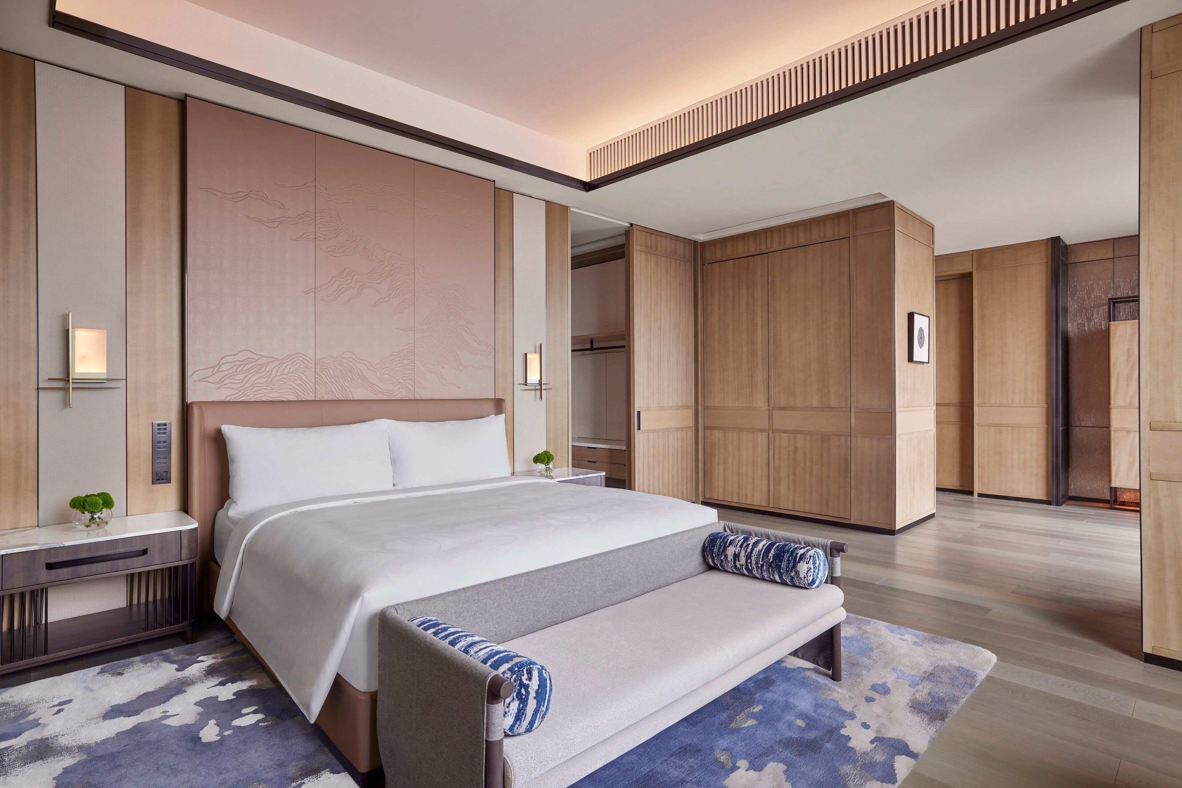 A modern hotel room with a large bed, bedside tables, a bench, and a wardrobe.