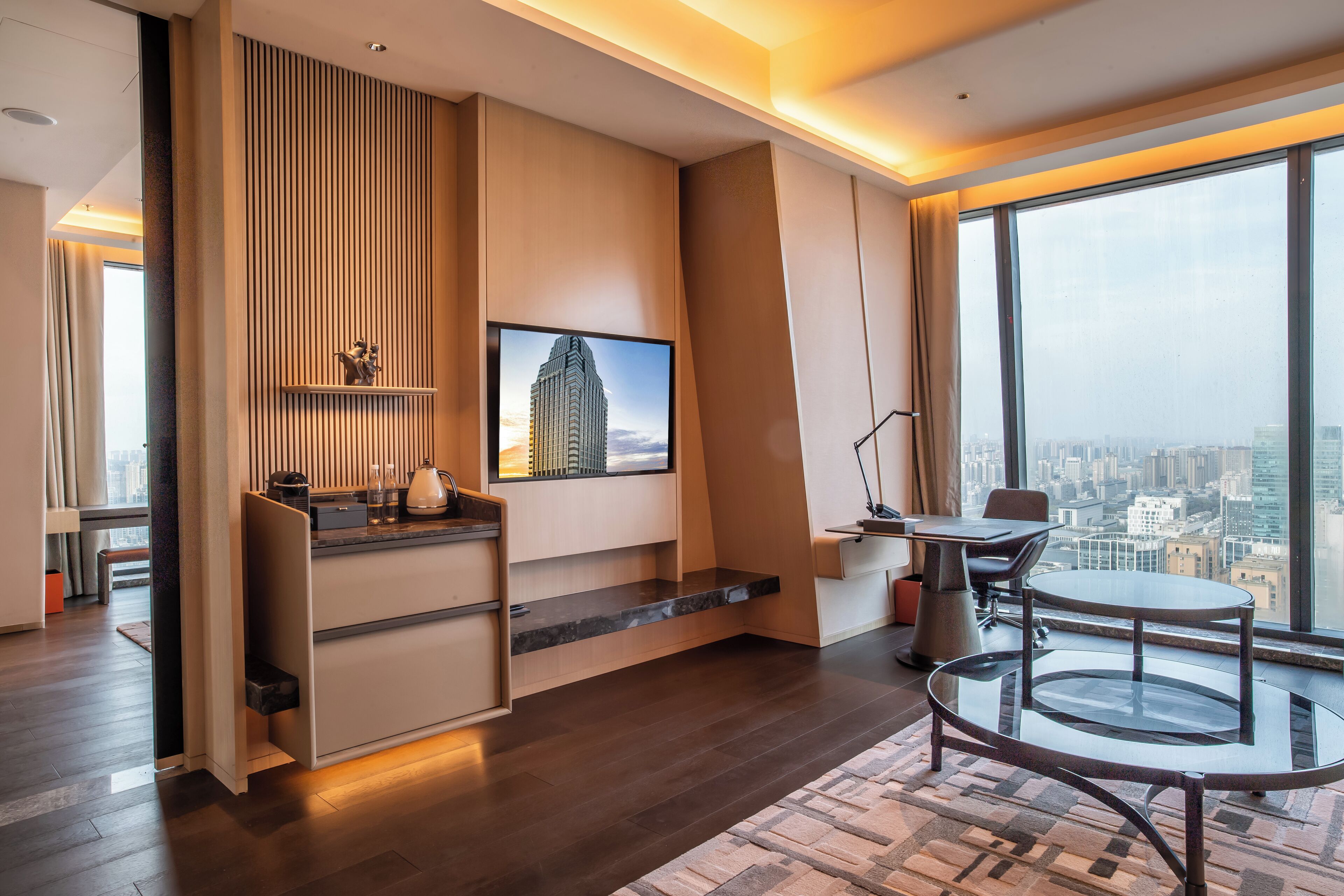 Una habitación de hotel moderna con un ventanal grande, un escritorio, una silla y una pequeña mesa.