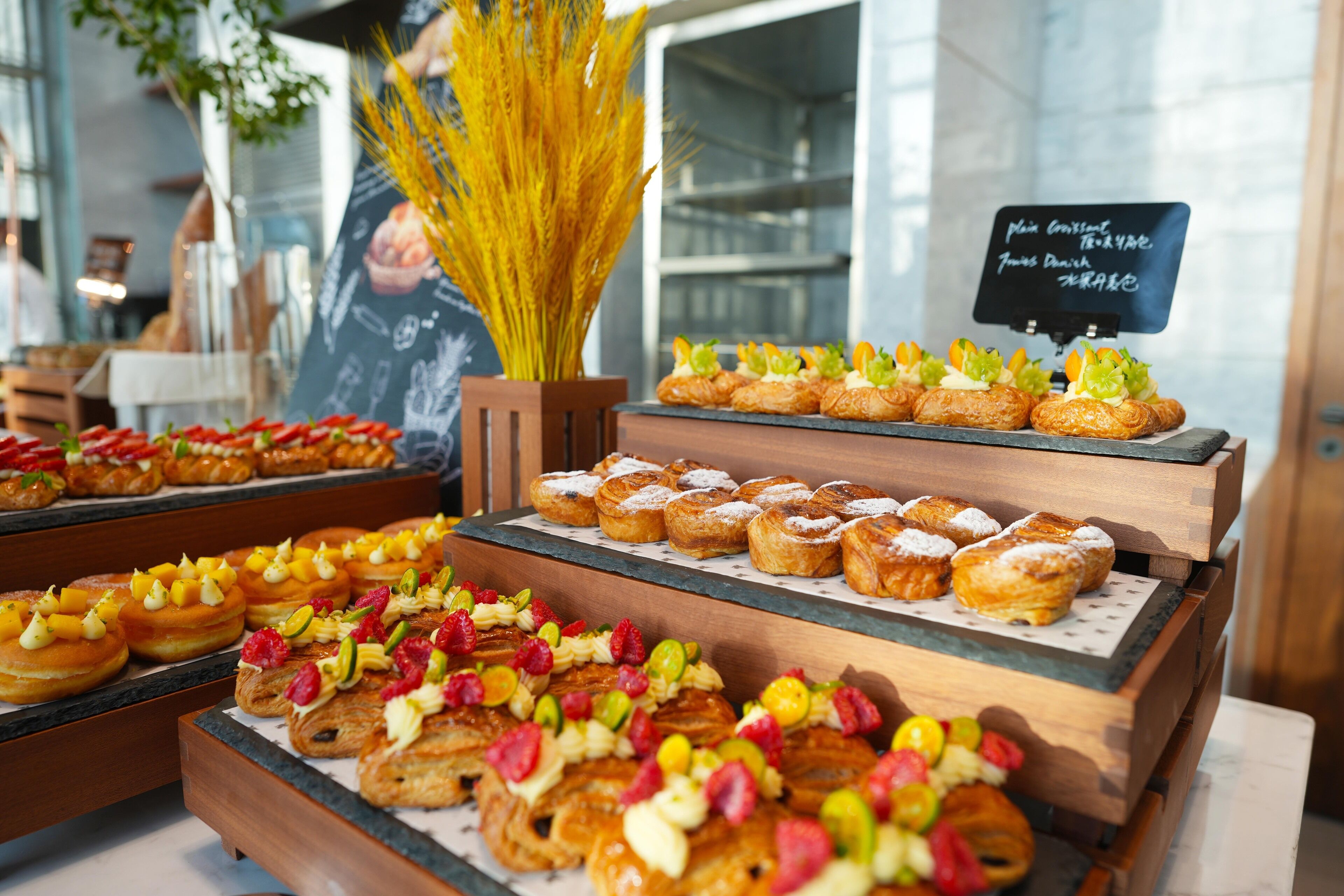 Una exhibición de diversos pasteles y postres, incluyendo croissants y hojaldres cubiertos de frutas y nueces, dispuestos sobre bases de madera.