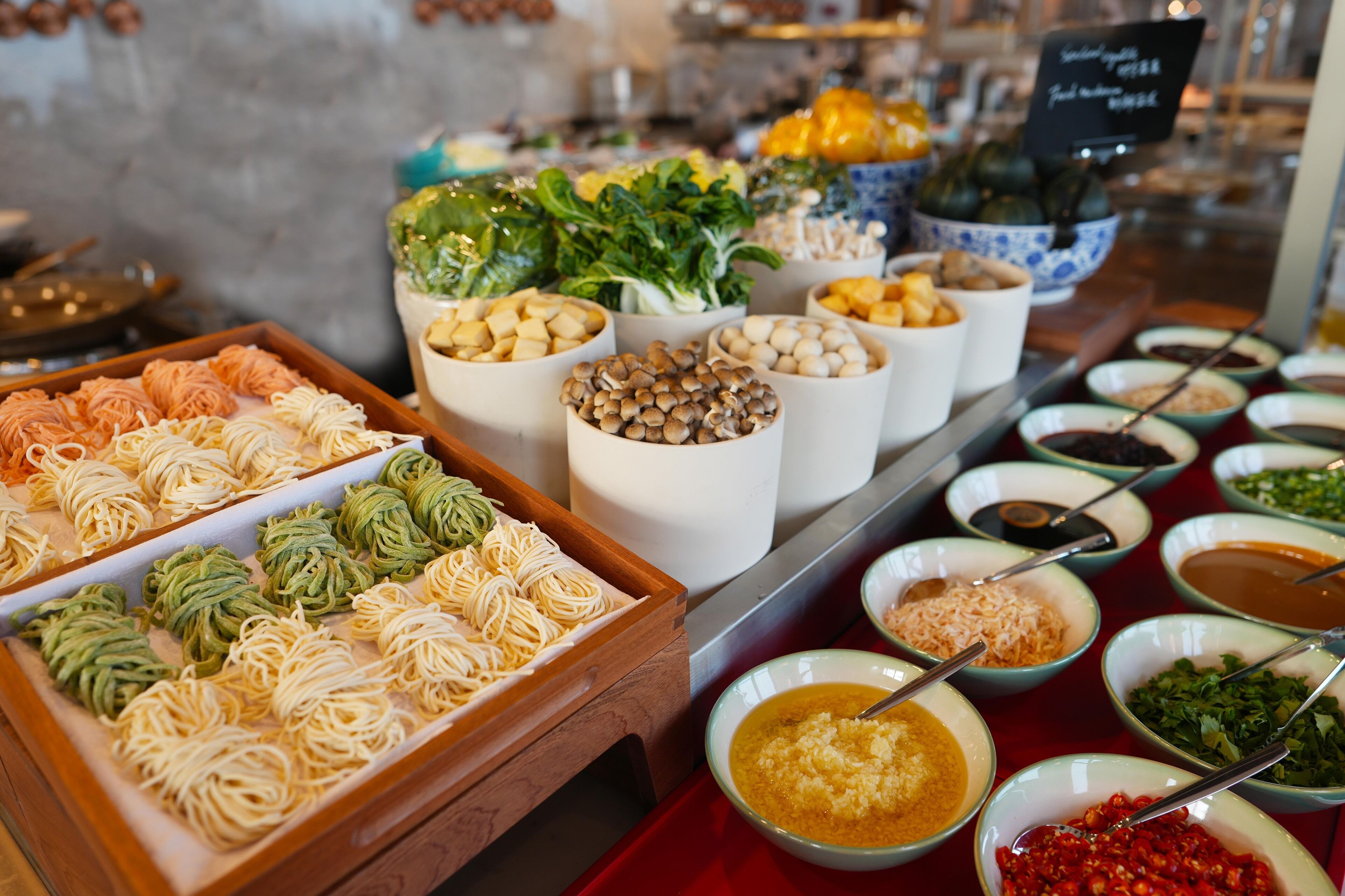 Un bufé con diversos alimentos, incluyendo fideos, verduras y salsas.