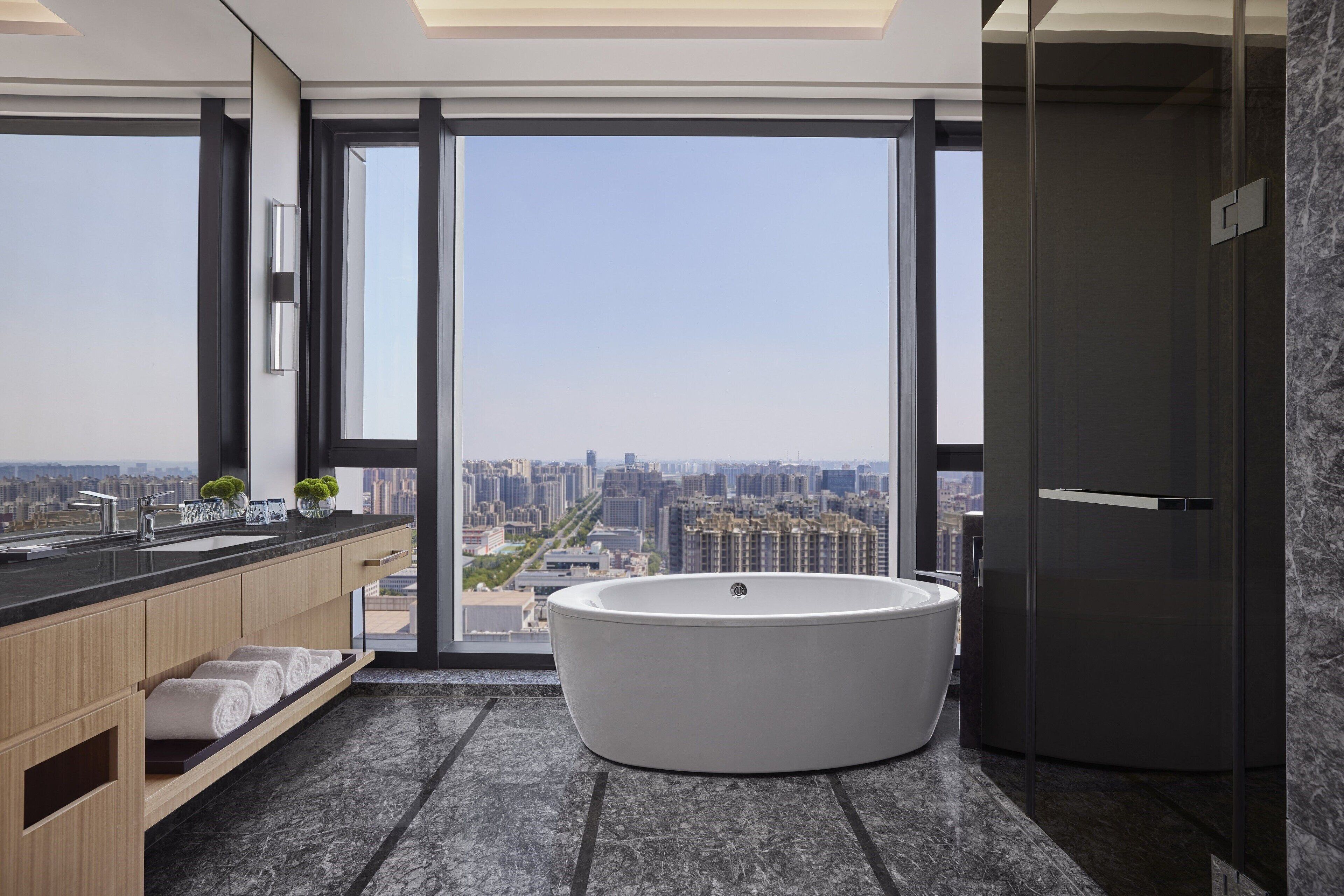Une salle de bain moderne dotée d’une grande baignoire, d’un meuble-lavabo et d’une grande fenêtre offrant une vue sur la ville.