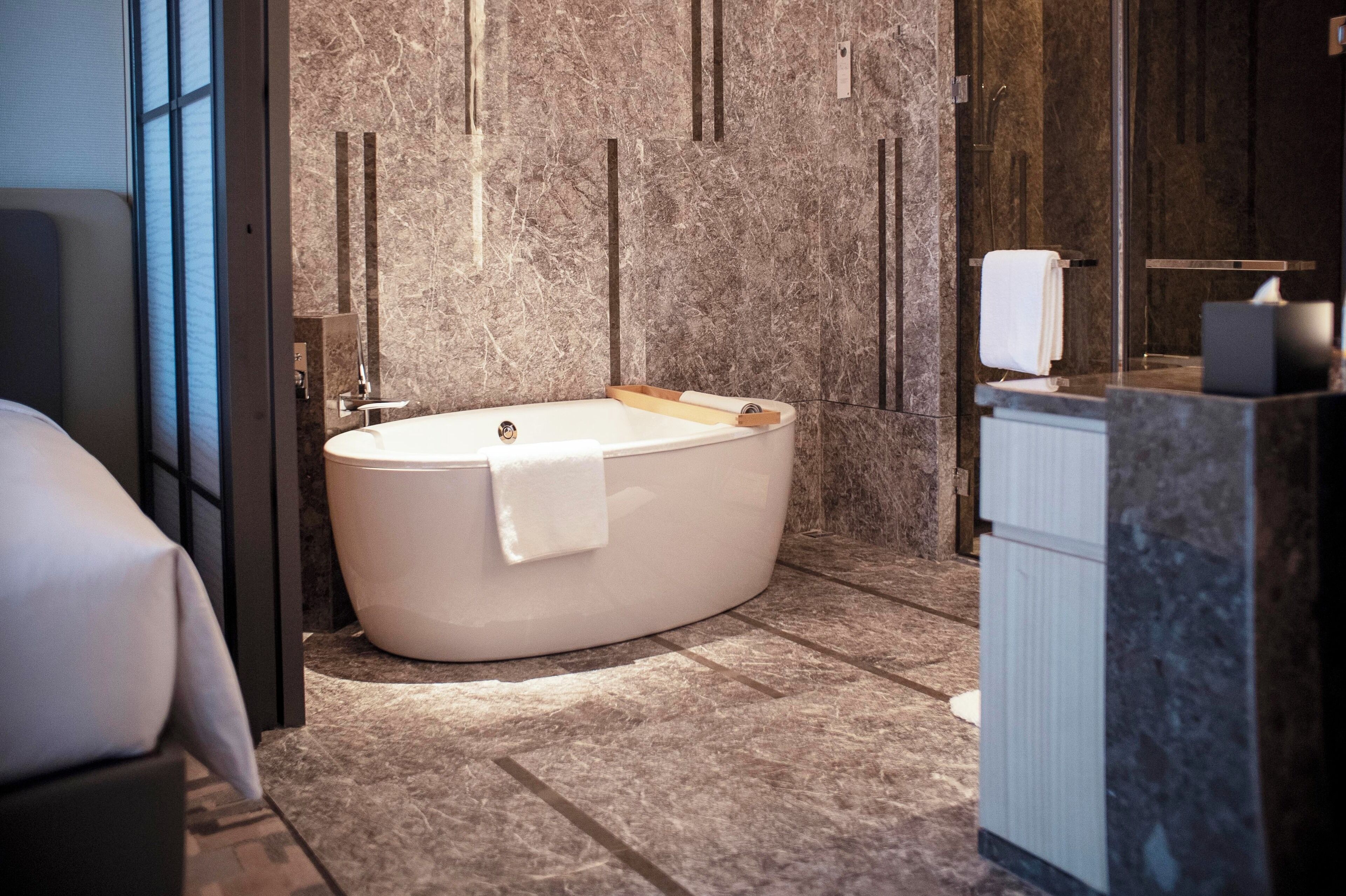 A modern bathroom with a freestanding bathtub, marble walls, and a glass shower enclosure.