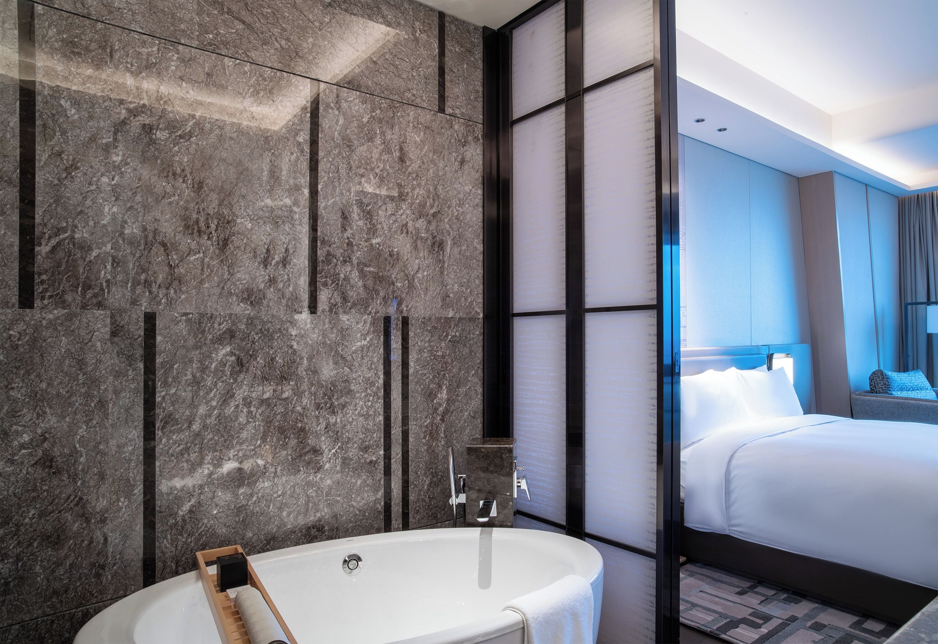 Un baño moderno con una bañera independiente, paredes de mármol y una cama grande con ropa blanca.