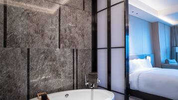Un baño moderno con una bañera independiente, paredes de mármol y una cama grande con ropa blanca.