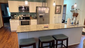 Una cocina moderna con encimeras de granito, electrodomésticos de acero inoxidable y taburetes de bar.