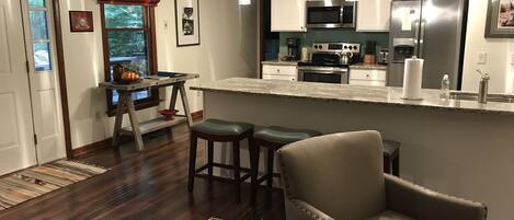 A modern kitchen with a central island, bar stools, and a dining area with a wooden table.