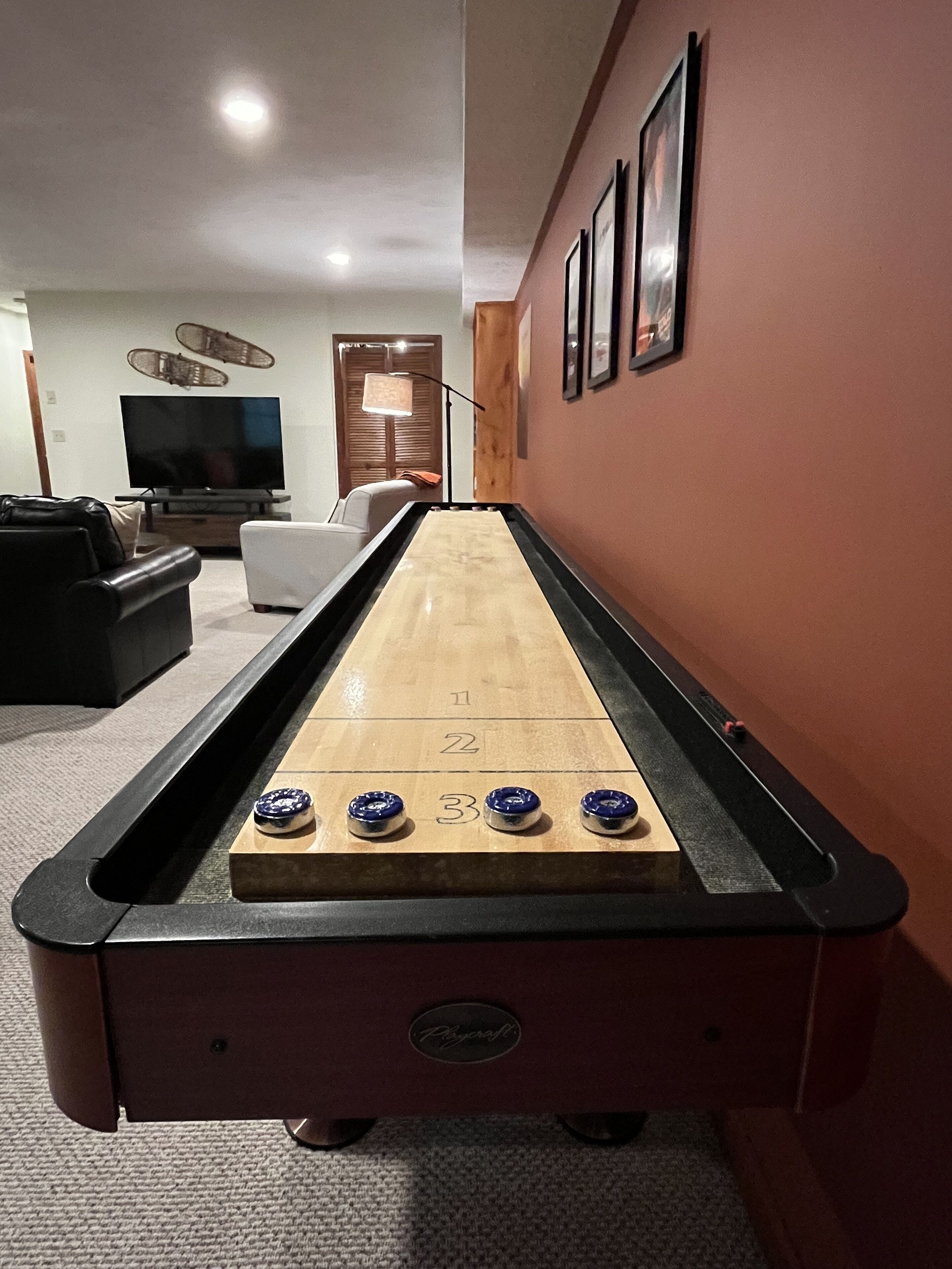Een jeu de boules tafel in een woonkamer, met een bank en een televisie op de achtergrond.
