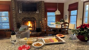 Una sala de estar acogedora con chimenea, un comedor con mesa y sillas, y una encimera de cocina con alimentos y bebidas.