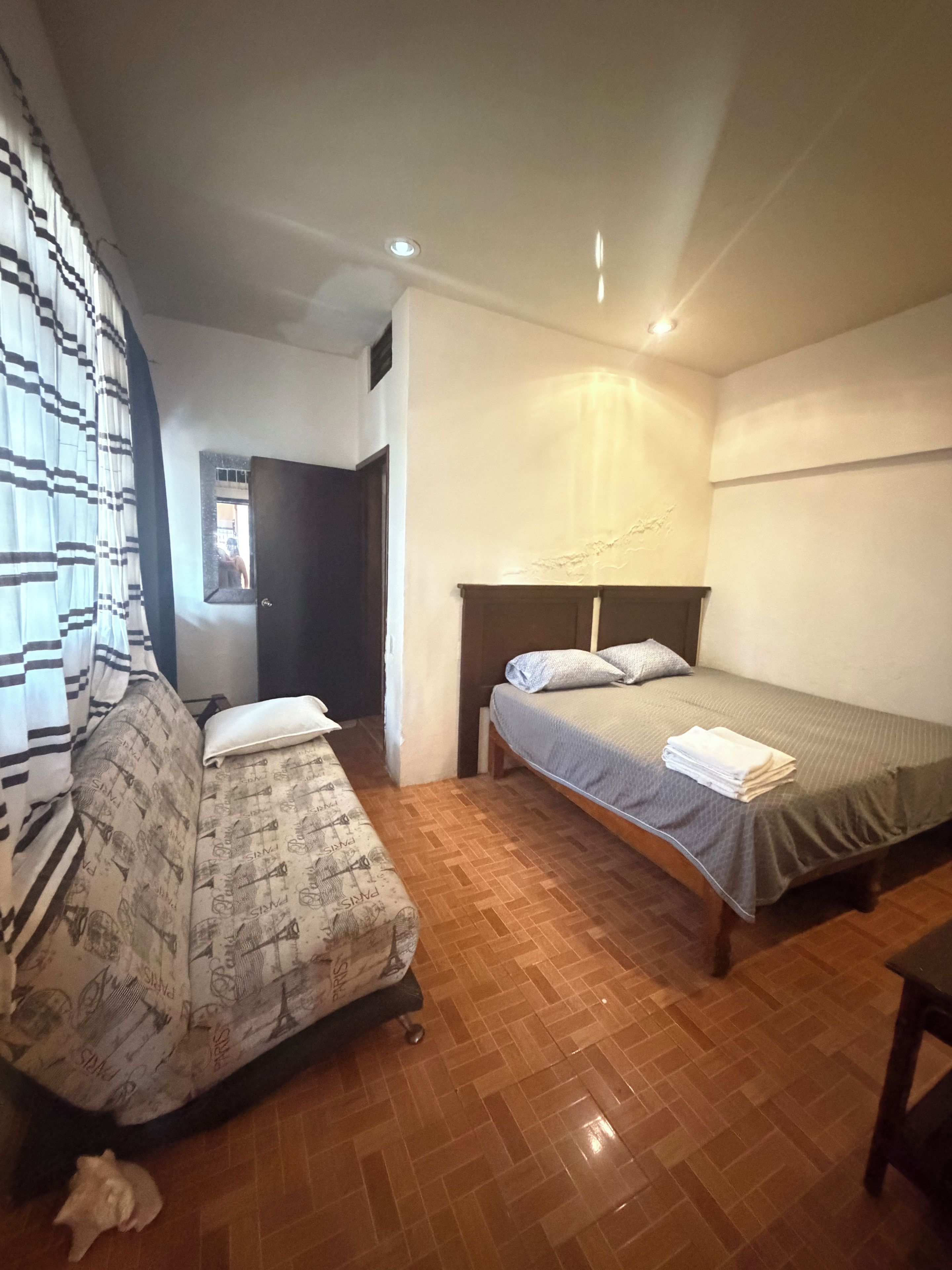 A bedroom with a bed, a sofa, and a wooden floor.