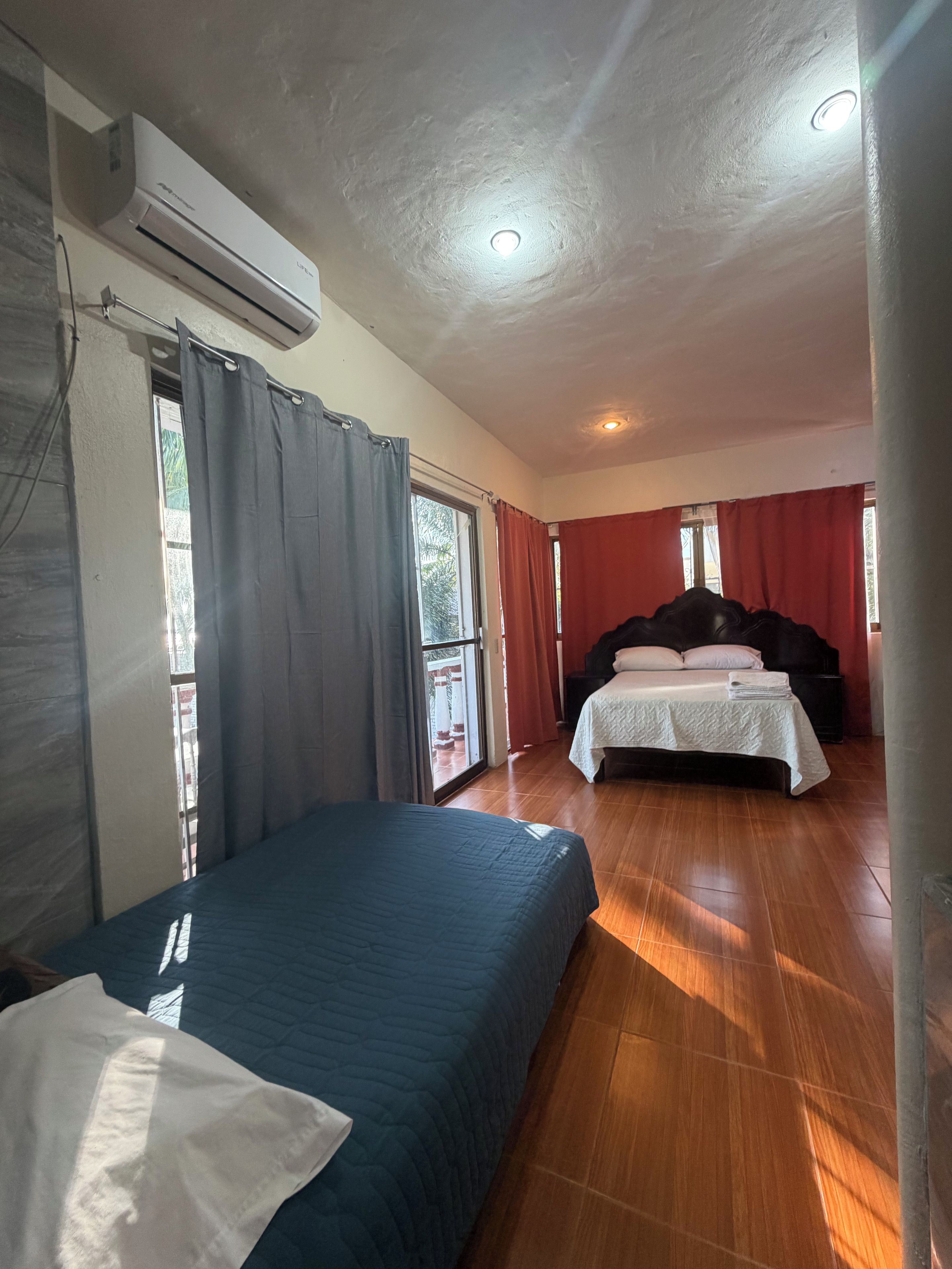 Habitación de hotel con una cama, una segunda cama, un equipo de aire acondicionado y una ventana con cortinas.