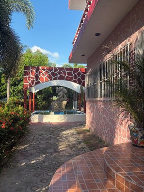 Une cour avec un chemin pavé de carreaux, une arche décorative et une fontaine.