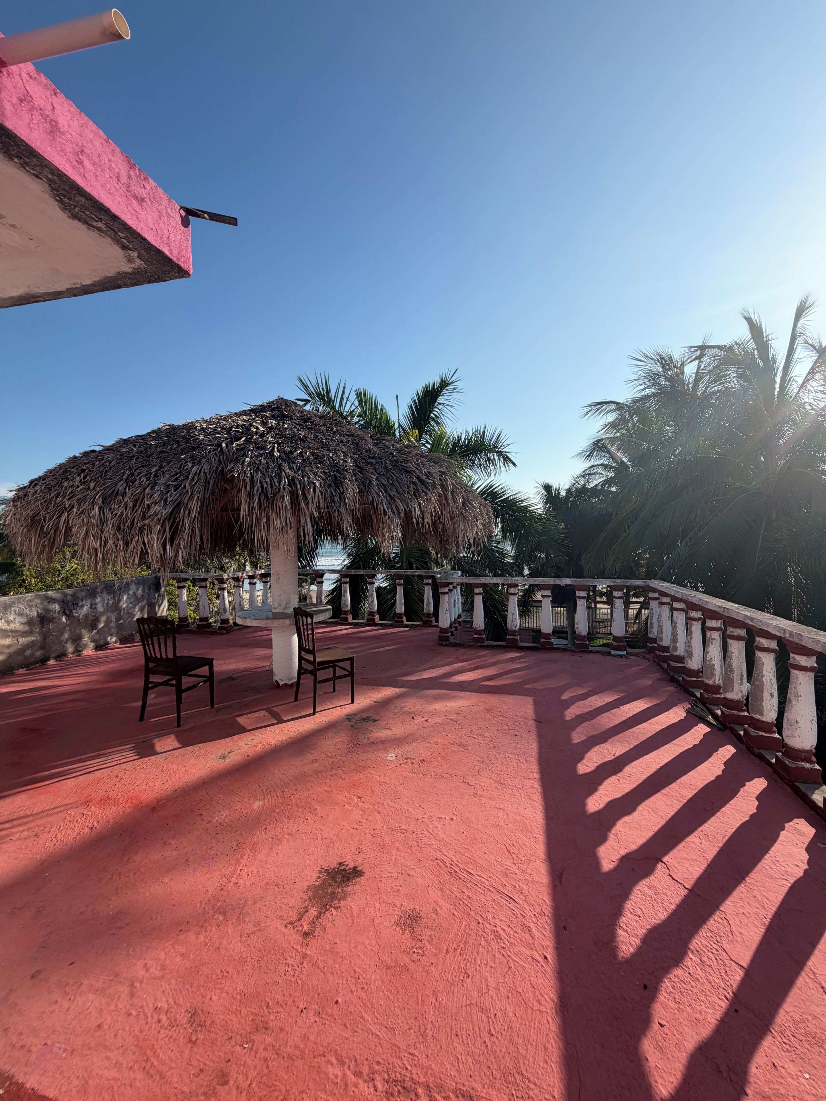 A red-tiled terrace with two chairs, a thatched-roof structure, and a white balustrade.