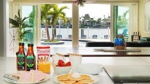 Una mesa de desayuno con té, jugo y pasteles, con vistas a una marina con barcos y palmeras.