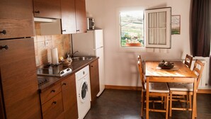 A kitchen with wooden cabinets, a built-in washing machine, a sink, and a dining table with chairs. - Apartamentos Corona (Comillas)