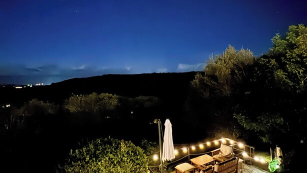 An outdoor patio area with stone flooring, wooden furniture, and string lights. - Apartamentos Corona (Comillas)