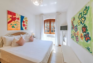 Een slaapkamer met een bed, kussens, een televisie en twee schilderijen.