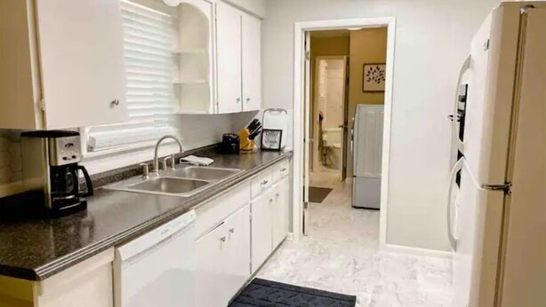 A modern kitchen with white cabinets, a coffee maker, a sink, and a refrigerator.