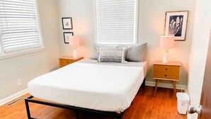A bedroom with a bed, two nightstands, a wooden floor, and a window with blinds.