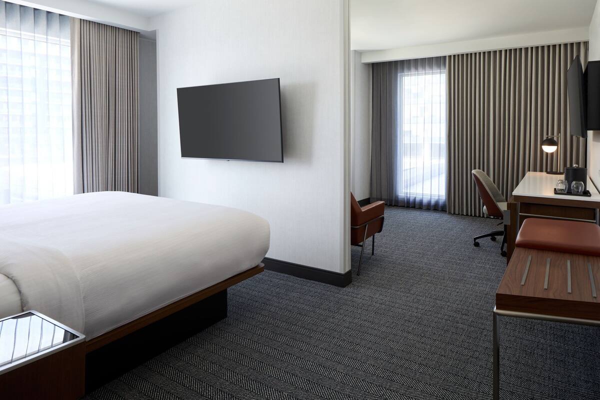 Habitación de hotel con una cama grande, un escritorio con silla, televisor y una ventana con cortinas.
