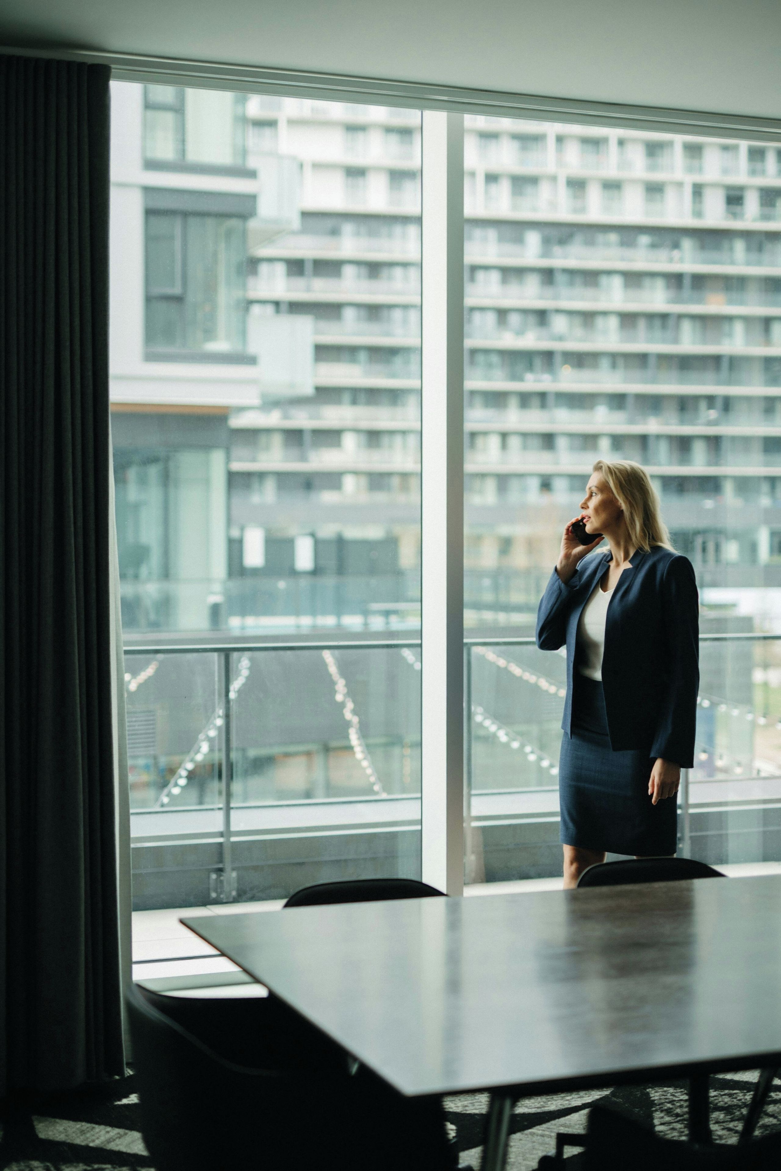A person standing by a large window in a room with a view of a cityscape.