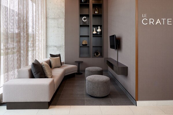 Una sala de estar moderna con un sofá, otomanas, un televisor y un mueble de estanterías con objetos decorativos.