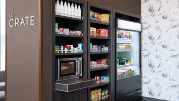 A kitchenette with a microwave, shelves stocked with snacks, and a refrigerator.