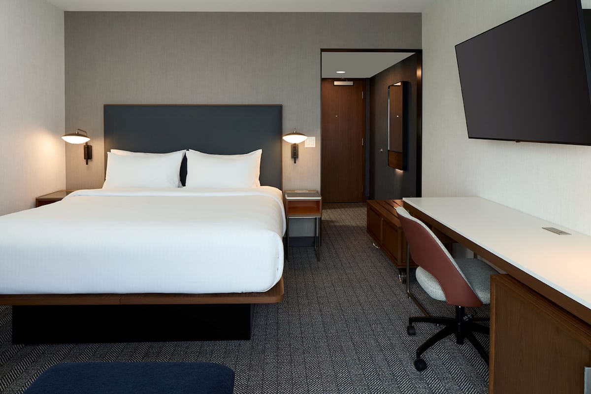 Habitación de hotel con una cama grande, mesitas de noche, un escritorio con silla y un televisor de pantalla plana montado en la pared.