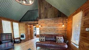 Een rustiek chaletinterieur met een houten vloer, een leren bank, een geruit fauteuil en een groot vloerkleed.