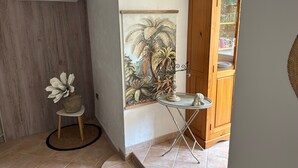 Un couloir avec une armoire en bois, un tableau représentant une végétation tropicale, une petite table sur laquelle se trouve un chandelier et un vase décoratif.