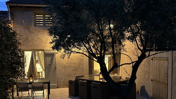 Un espace patio aménagé avec du mobilier d’extérieur, un arbre et un bâtiment doté de fenêtres et de volets.