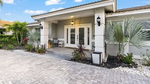 Una casa moderna con porche cubierto, puerta con paneles de vidrio y un jardín cuidado con diversas plantas.