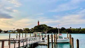 Un muelle con un barco amarrado, un faro al fondo y una masa de agua tranquila.