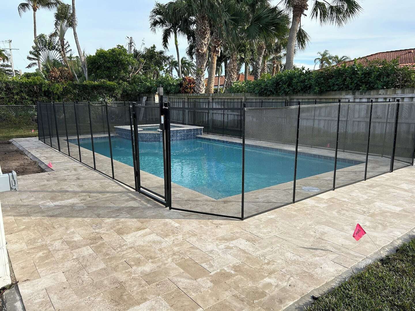 A rectangular swimming pool with a black fence, surrounded by a stone patio.
