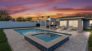 Un patio trasero con piscina, un porche cubierto y una casa con grandes ventanales.