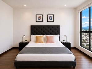 Un dormitorio moderno con una cama grande, dos mesitas de noche, un cabecero tapizado negro y dos cuadros enmarcados en la pared.