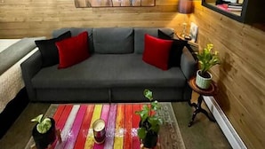 A cozy living room with a gray sofa, red cushions, a colorful striped coffee table, and a painting of flowers on the wall.