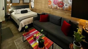 A cozy room with a bed, a sofa, a colorful coffee table, and a large painting on the wall.