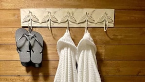 Two white bathrobes hanging on a wooden wall with a wooden floor.