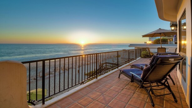 Un balcone con vista sul tramonto sull'oceano, arredi da esterno e una ringhiera.
