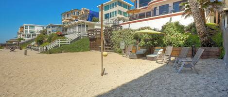 A beachfront property with multiple buildings, a sandy beach, and outdoor seating areas.
