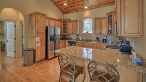 A kitchen with wooden cabinets, granite countertops, a stainless steel refrigerator, and a bar area with two chairs. - Lakefront Cottage with Private Dock on Norris Lake (Sharps Chapel)
