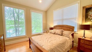 A bedroom with a large bed, two windows with blinds, a nightstand with a lamp, and a dresser. - Lakefront Cottage with Private Dock on Norris Lake (Sharps Chapel)